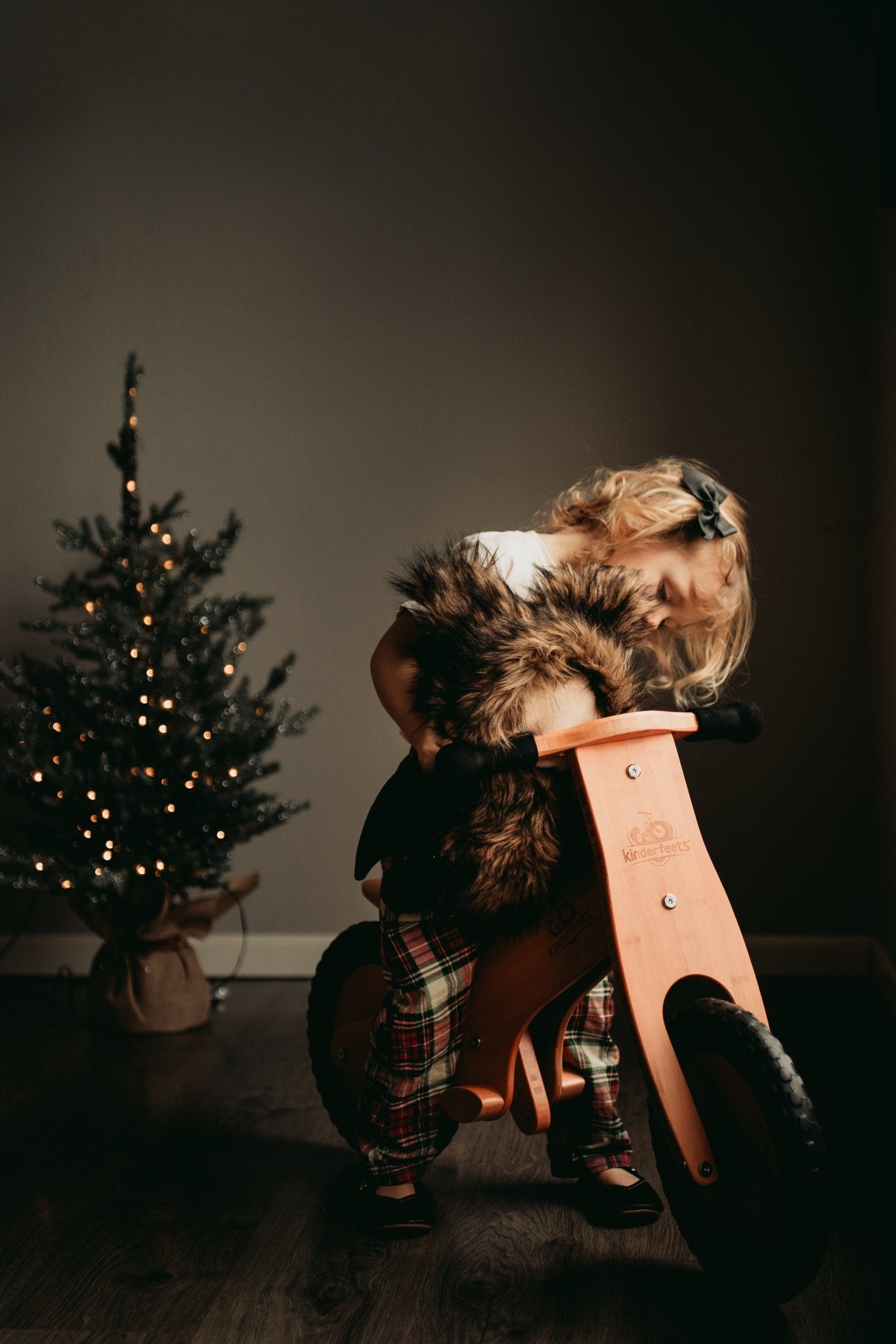 Toddler sitting on Kinderfeets Bamboo balance bike while holding her furry friend. 