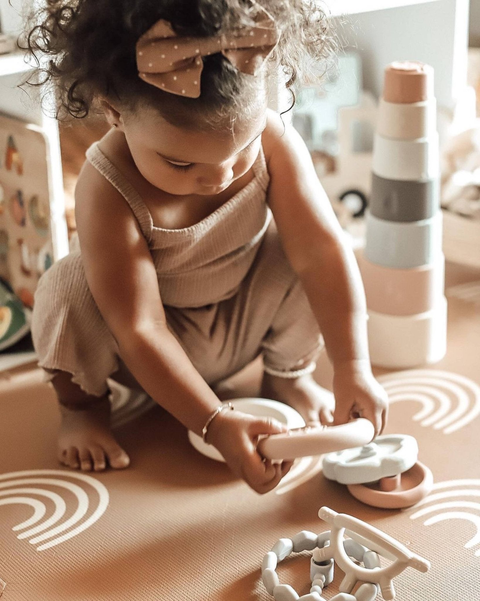 Toddler playing with silicone stacking rings on rug.