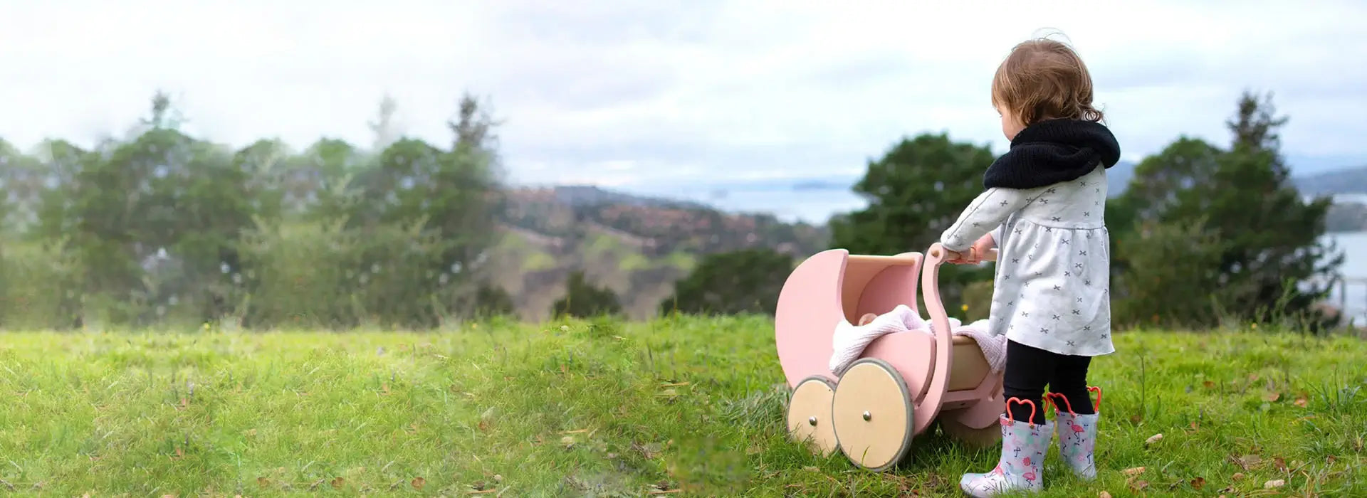 An adorable child playing with a pink stroller in a beautiful field of flowers