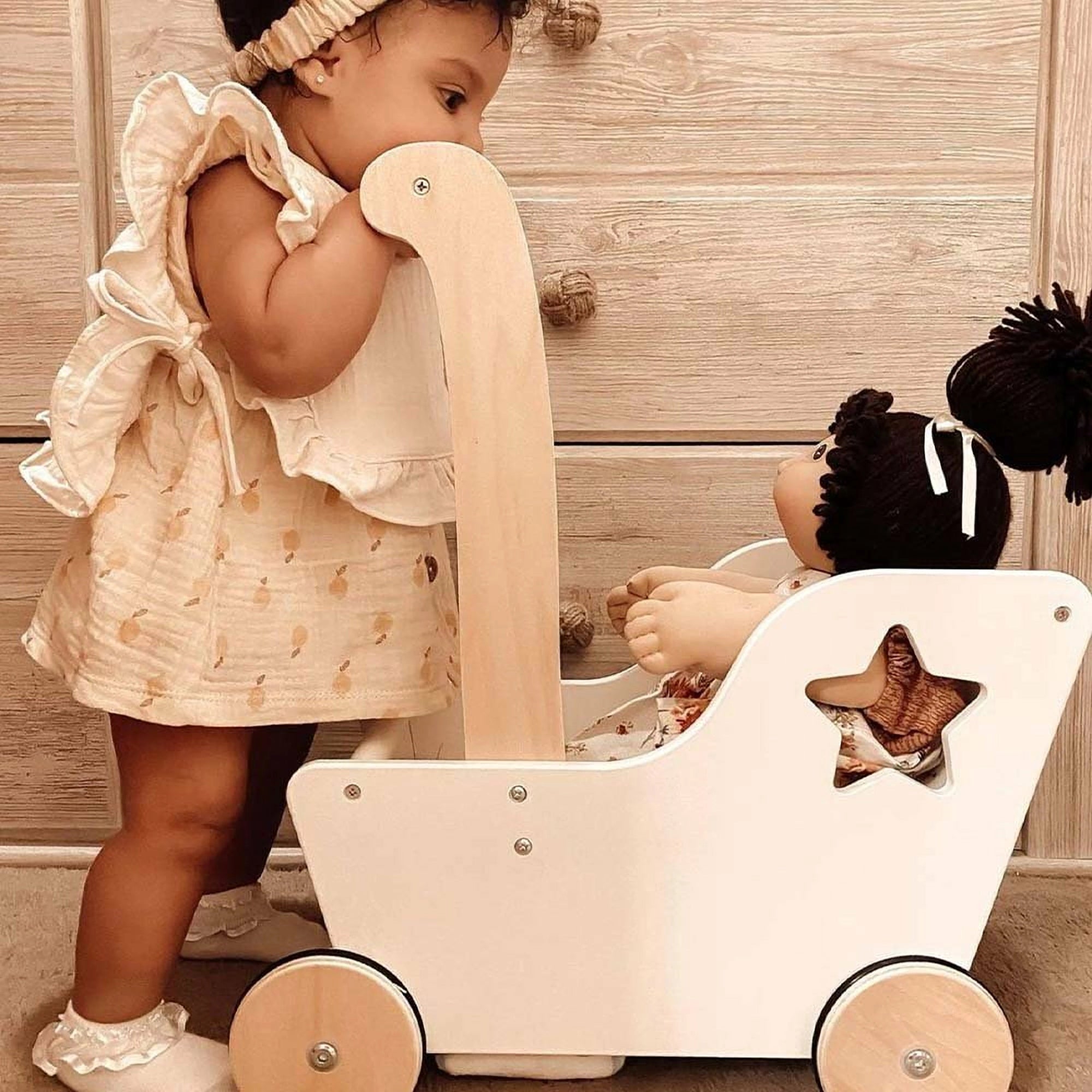 Ali + Oli Muslin Cotton Baby Bib in Ivory placed next to a doll in a wooden toy wagon