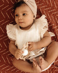 Ali + Oli Muslin Cotton Ruffle Baby Bib in Ivory worn by a baby with a white headband