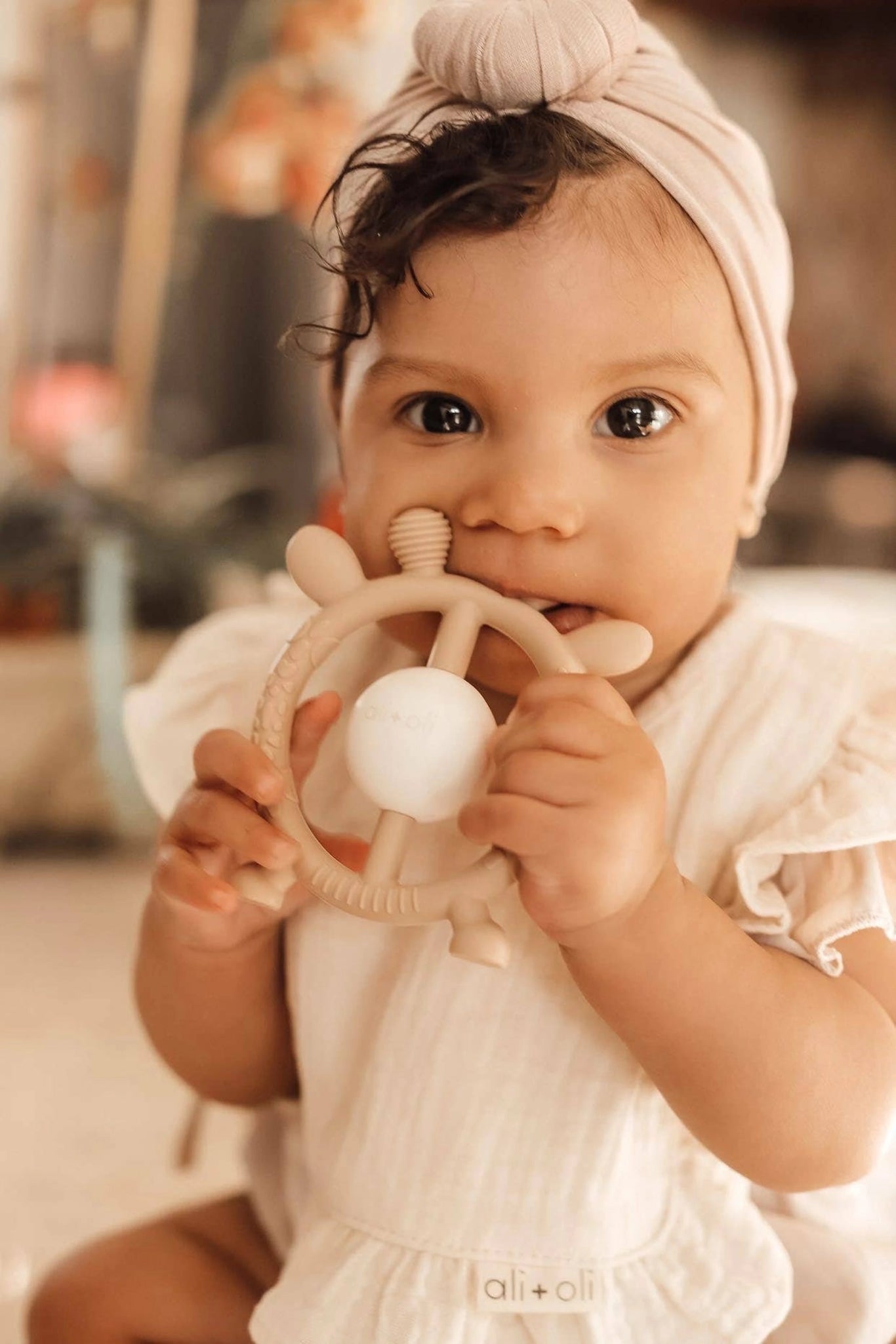 Ivory Ali + Oli Muslin Cotton Ruffle Baby Bib held by a baby with a wooden toy