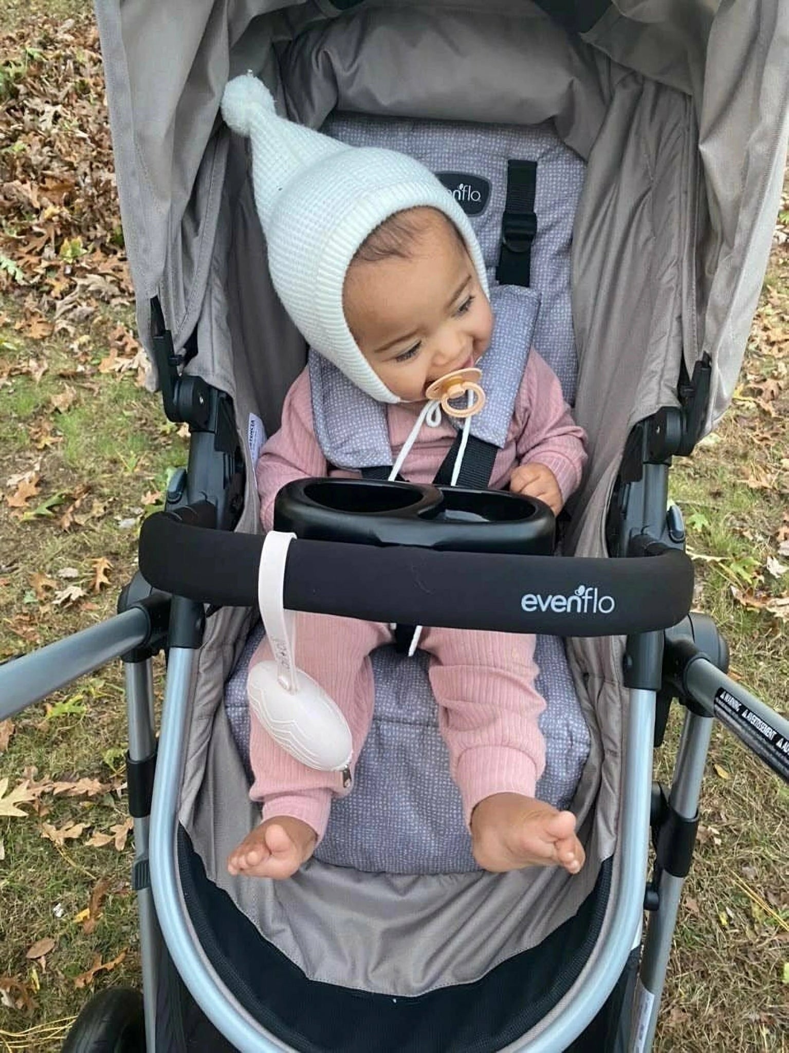 Close-up of a baby in a stroller with the ALI + OLI pacifier holder case nearby