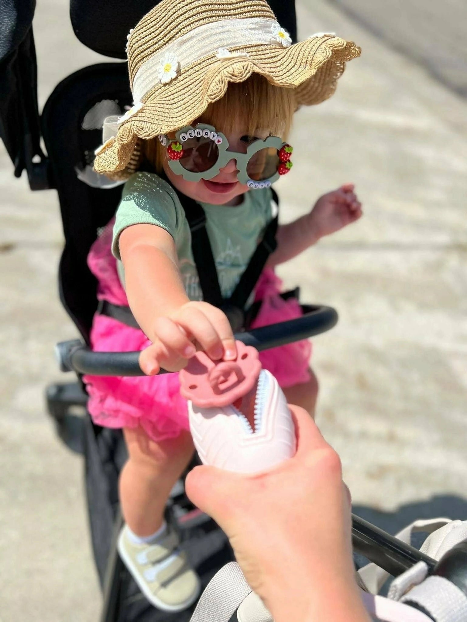 Stroller equipped with an ALI + OLI pacifier holder beside a baby in a hat