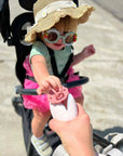 Stroller equipped with an ALI + OLI pacifier holder beside a baby in a hat