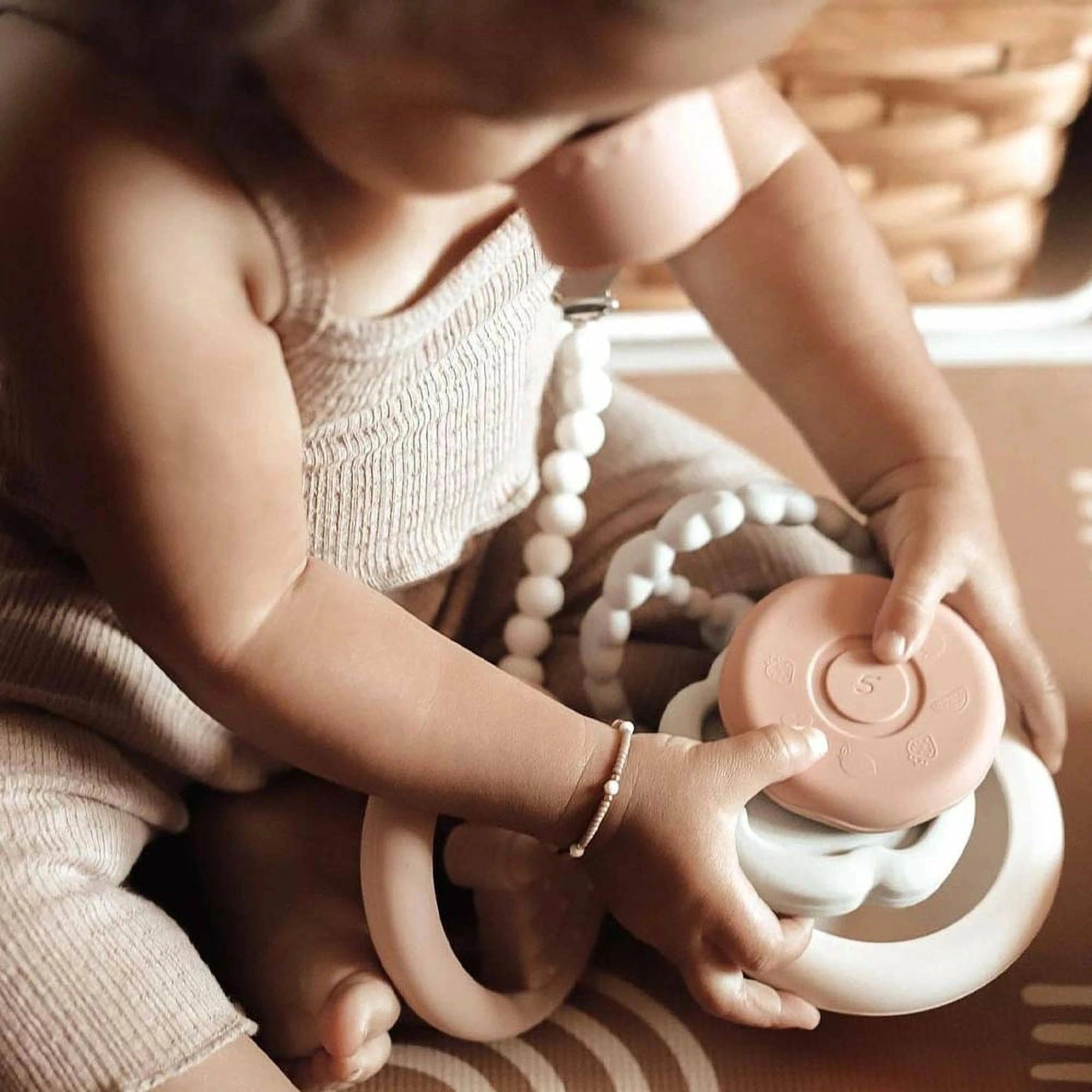 An infant engaging with the Ali + Oli Soft Silicone Stacking Ring Tower on a soft rug