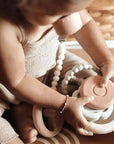 An infant engaging with the Ali + Oli Soft Silicone Stacking Ring Tower on a soft rug