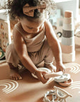 A toddler girl playing with the Ali + Oli Soft Silicone Stacking Ring Tower on a patterned rug