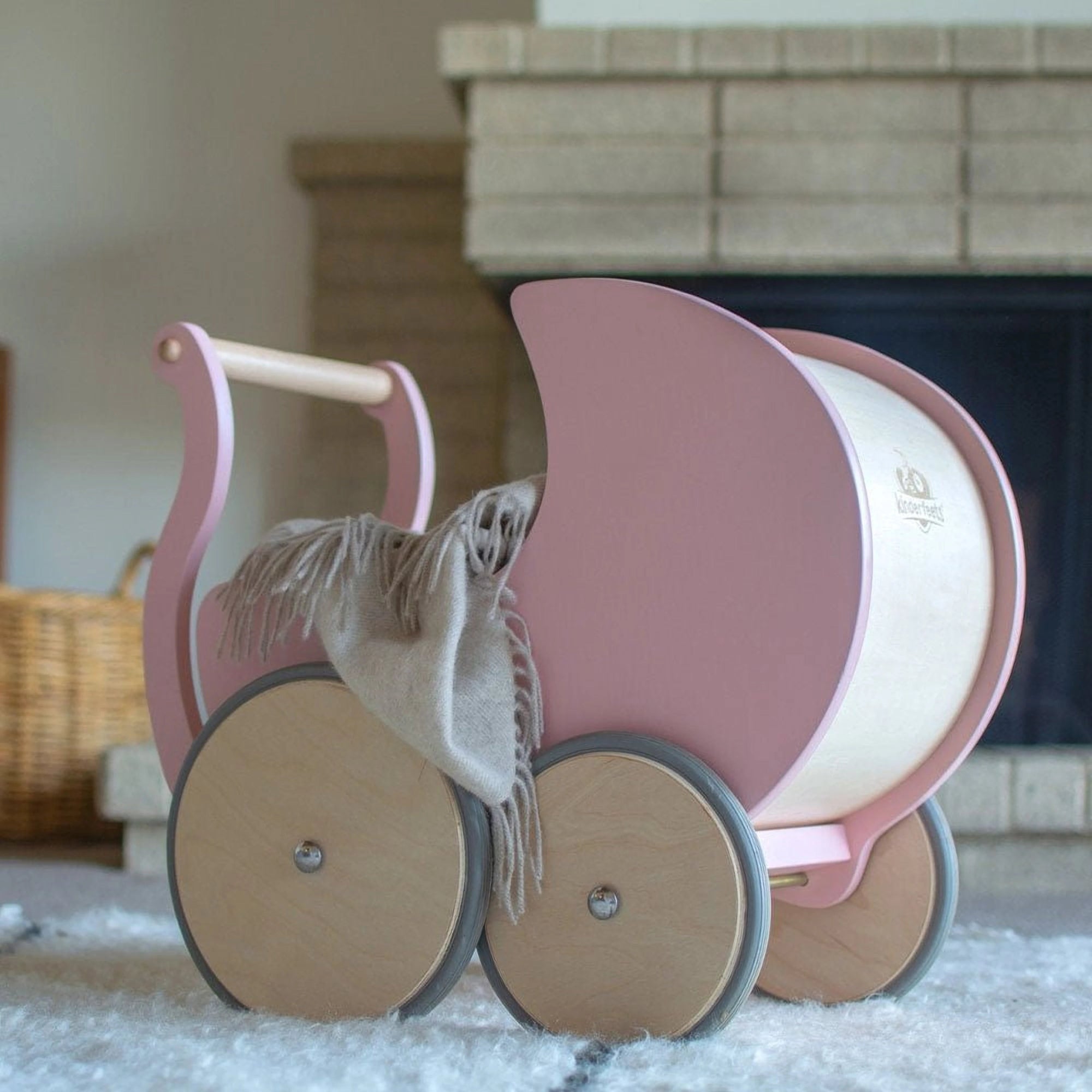 Rose Kinderfeets wooden pram with a cozy blanket inside, placed on the floor