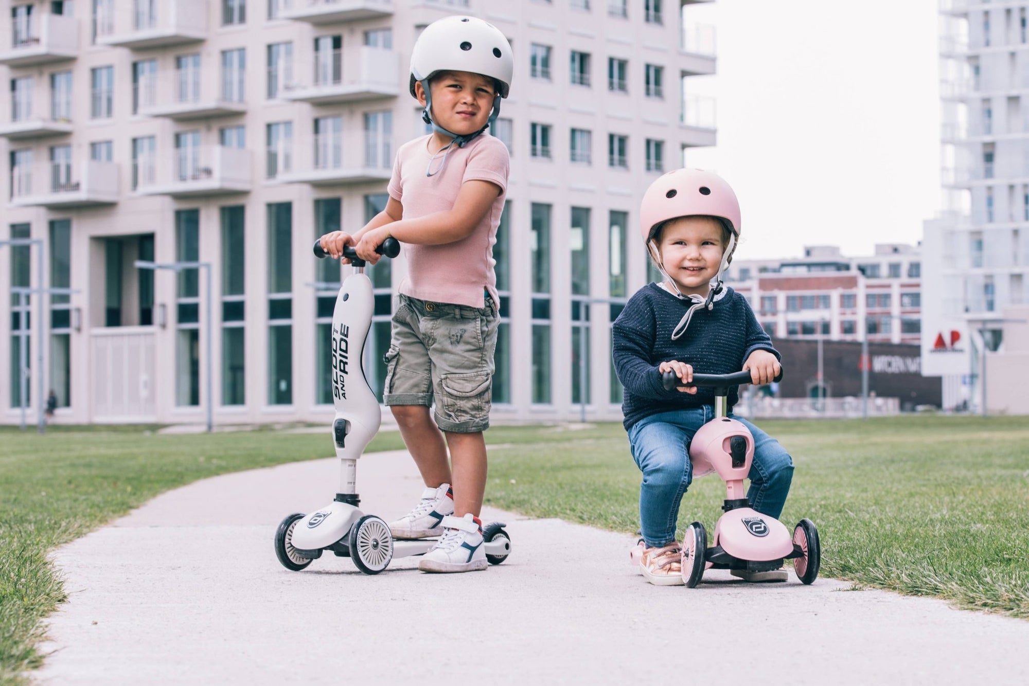 Siblings having fun together riding their Scoot & Ride scooters near a building