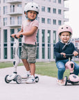 Siblings having fun together riding their Scoot & Ride scooters near a building