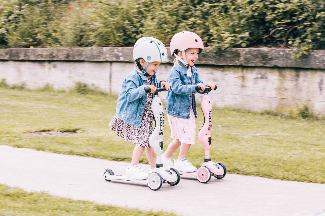 Two kids safely wearing helmets while riding their Scoot &amp; Ride scooters outdoors