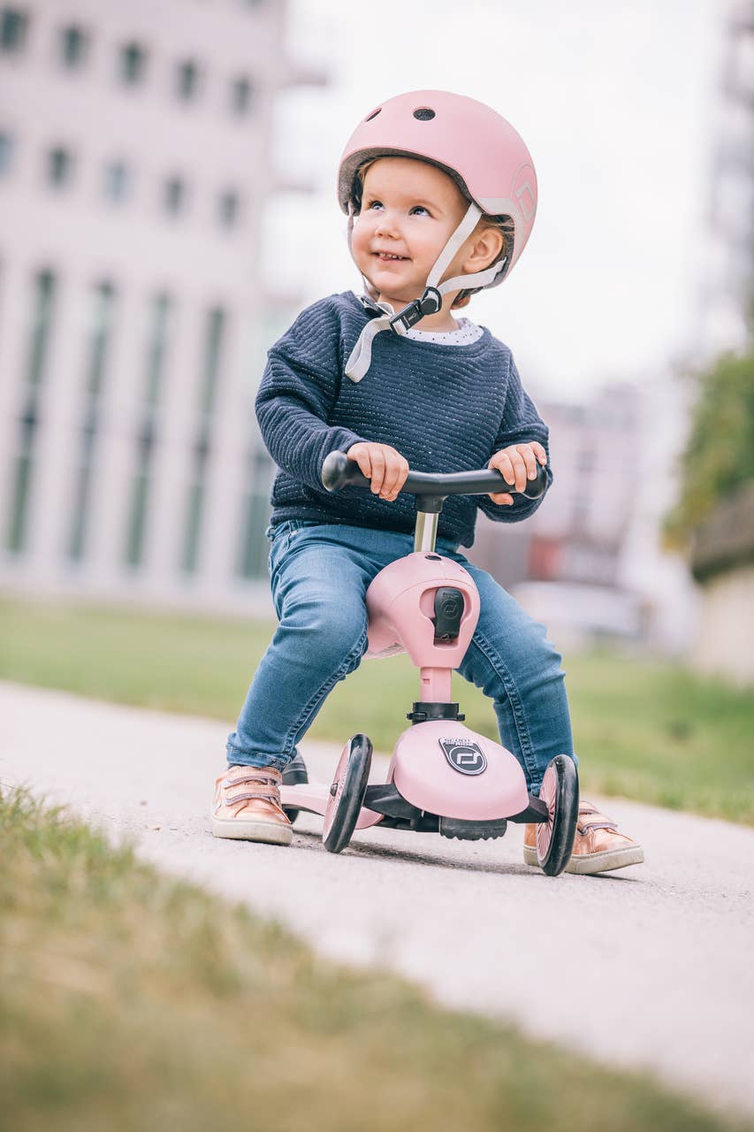 Young girl wearing a safety helmet and riding her rose Highwaykick 1 scooter