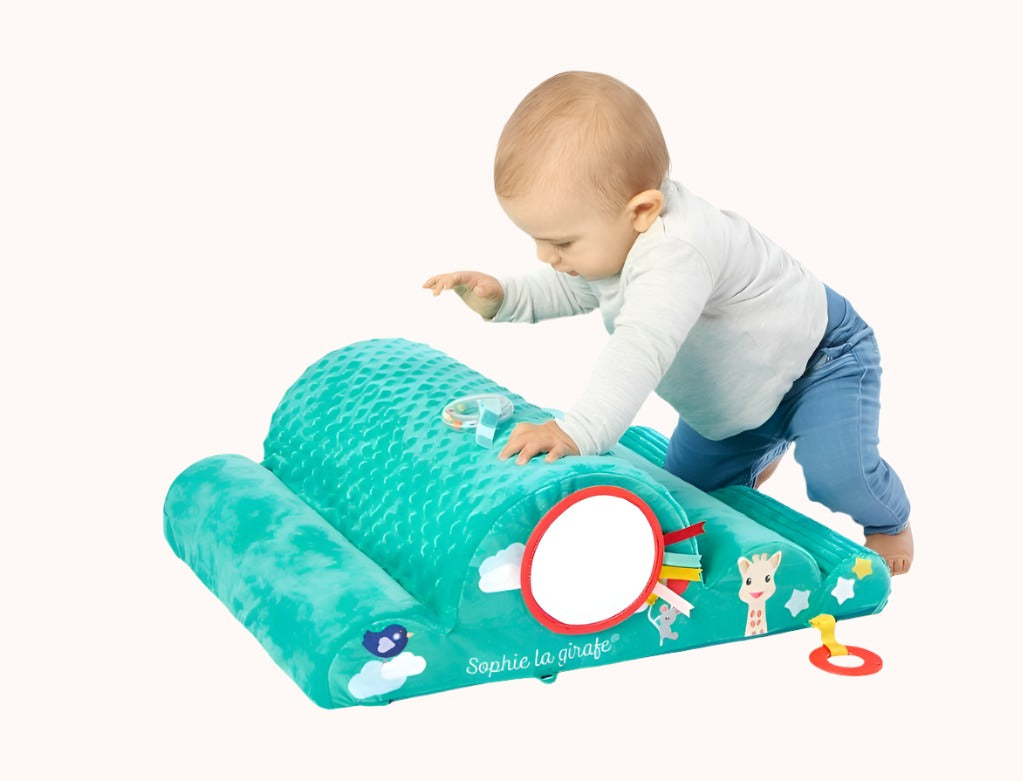 Infant playing with Sophie La Girafe toy on a green and white striped mat