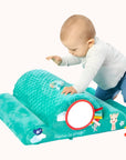 Infant playing with Sophie La Girafe toy on a green and white striped mat