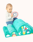 Toddler seated on a green Sophie La Girafe playmat with attached mirror toy