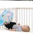 Baby lying in a crib using his feet to play with Sophie la Girafe Touch & Play Board 