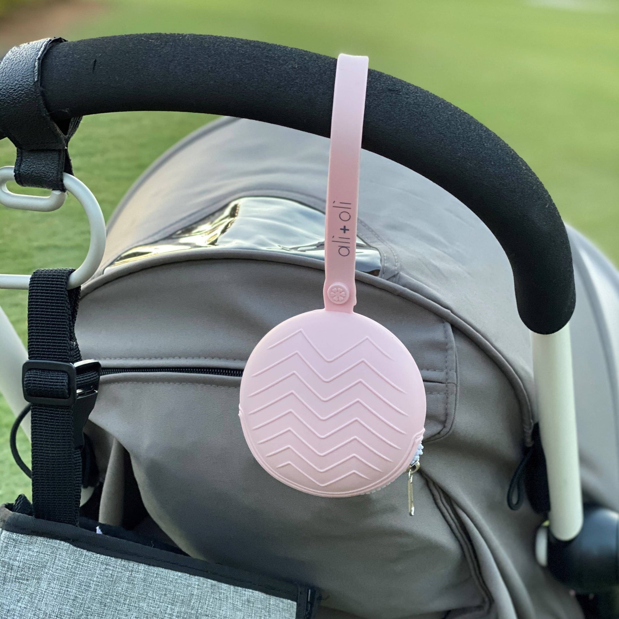 ALI + OLI pacifier holder attached to a stroller in pink color