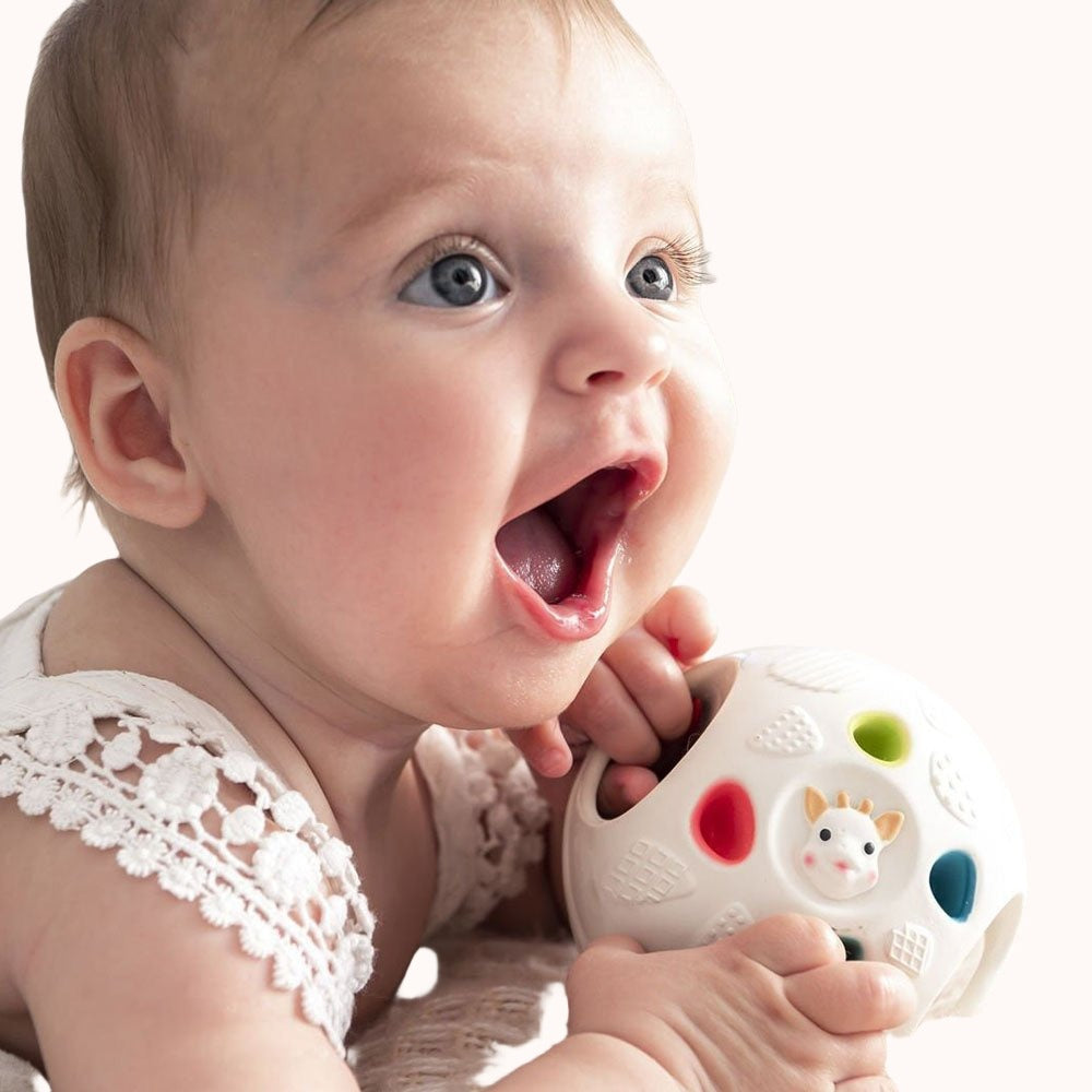 Infant engaging with a Sophie la Girafe So&#39;Pure Senso&#39;ball on a soft surface